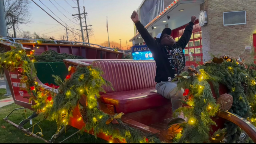 Kid sits in front of Santa's sleigh with arms in air