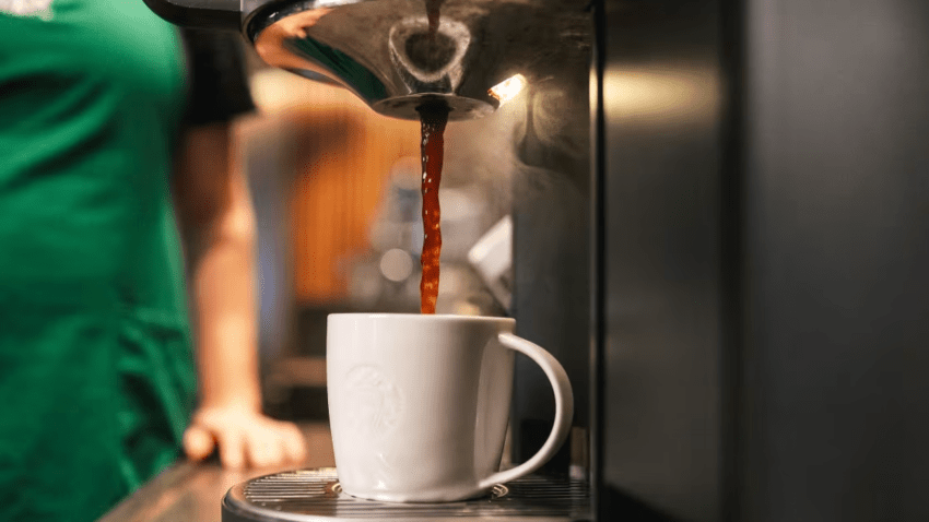 A Starbucks barista fills up a cup of coffee in a ceramic mug.