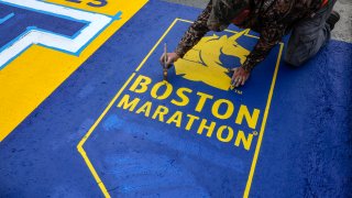 An employee of Mission Turf Services works on painting the starting line for the 129th Boston Marathon